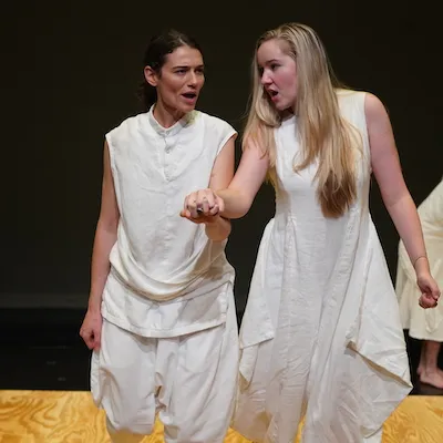 Two young women dressed in white, one leads the other by the hand