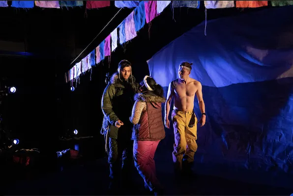 3 people stand and talk on a stage decorated with strings of flags