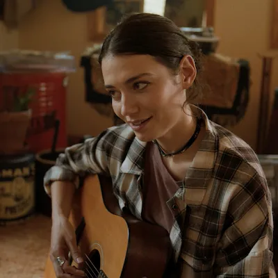 A young woman sits playing an acoustic guitar