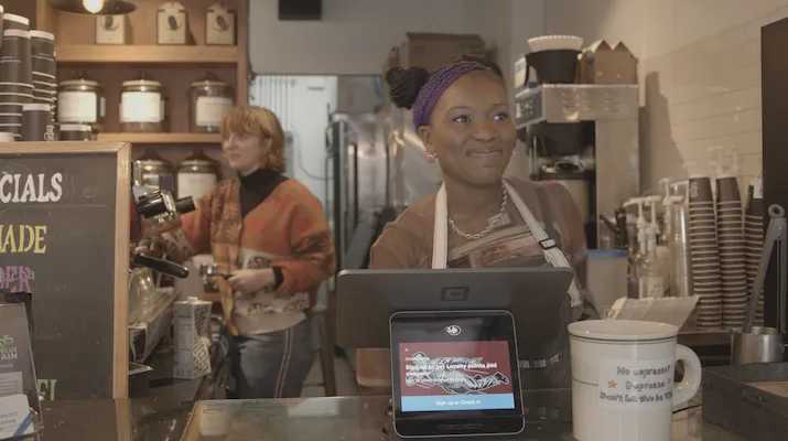 A young woman smiles behind the register of a coffee shop